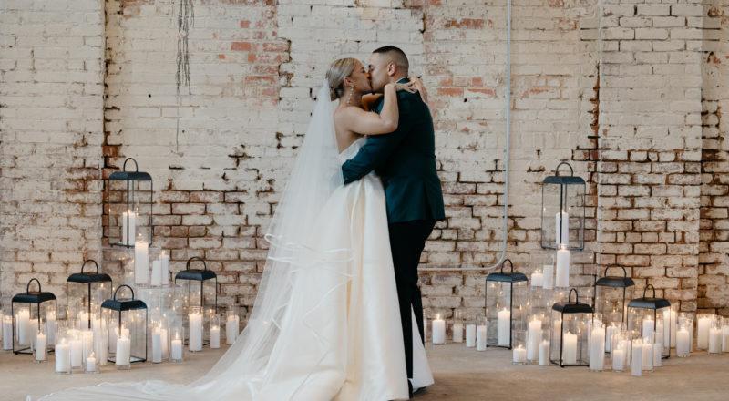 Wedding couple kissing with an industrial brick background and surrounded by candles